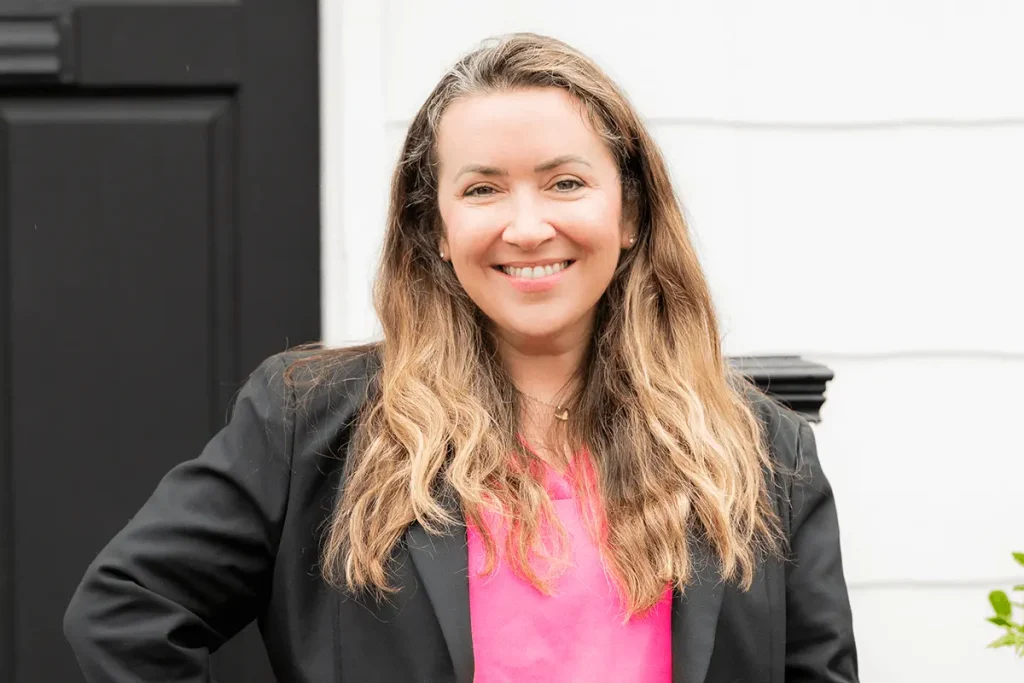 Confident professional woman standing outside an office building, smiling and wearing a black blazer over a white blouse.