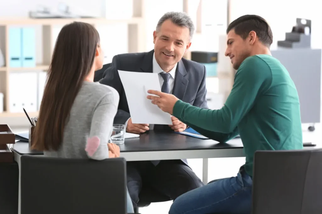 A couple sitting with an immigration attorney, discussing sponsorship paperwork for a green card application.