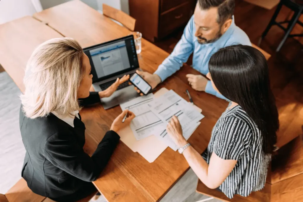 A couple meeting with an advisor at a desk, reviewing financial and legal documents related to immigration risks.