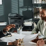 A couple sits across a desk from an immigration attorney, reviewing paperwork together during a consultation in a professional office setting.