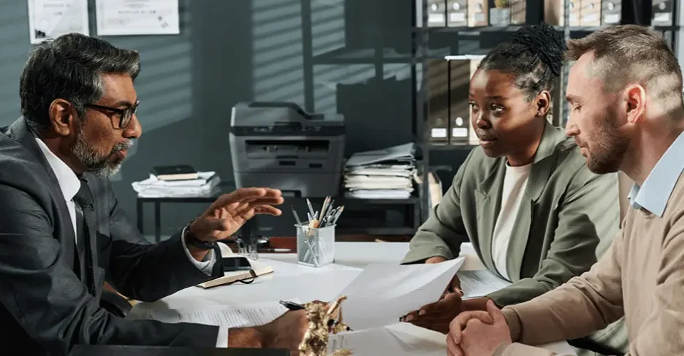 A couple sits across a desk from an immigration attorney, reviewing paperwork together during a consultation in a professional office setting.