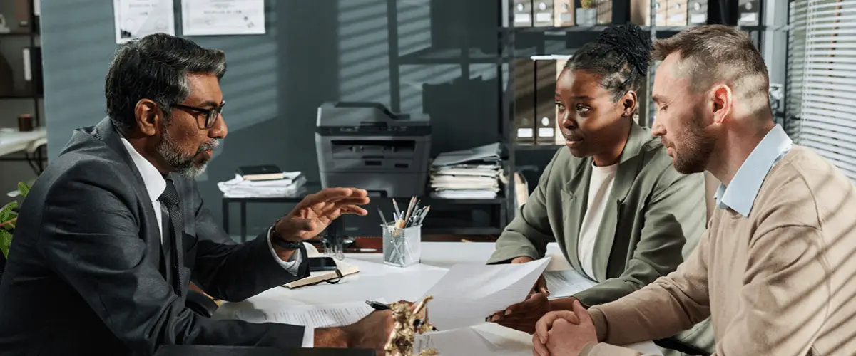 A couple sits across a desk from an immigration attorney, reviewing paperwork together during a consultation in a professional office setting.
