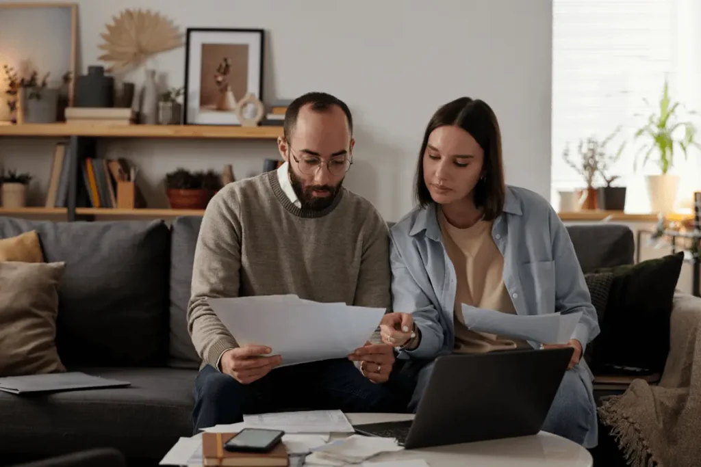 A couple sitting across from an advisor at a desk with a laptop and papers, discussing legal documents and immigration matters.