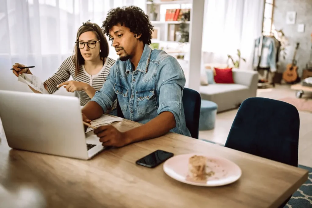 A worried couple sitting at a kitchen table with a laptop and papers, planning their immigration process and future decisions.