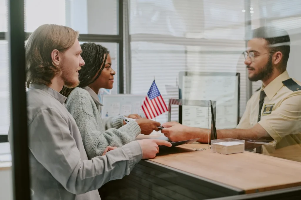 Couple submitting documents to immigration officer at counter with American flag visible