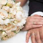 Newlywed couple showing wedding rings and bridal bouquet after marriage ceremony