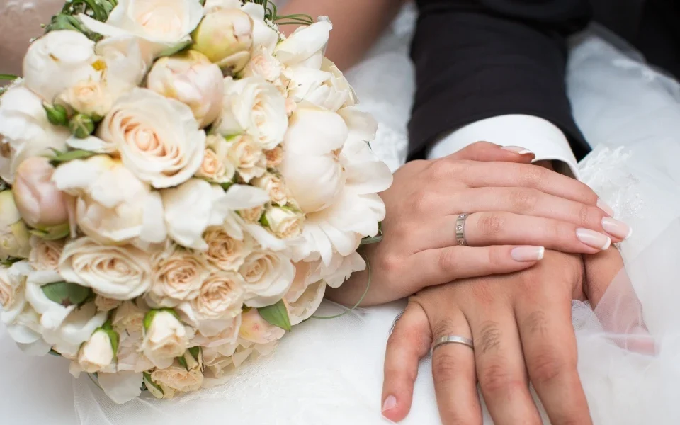 Newlywed couple showing wedding rings and bridal bouquet after marriage ceremony