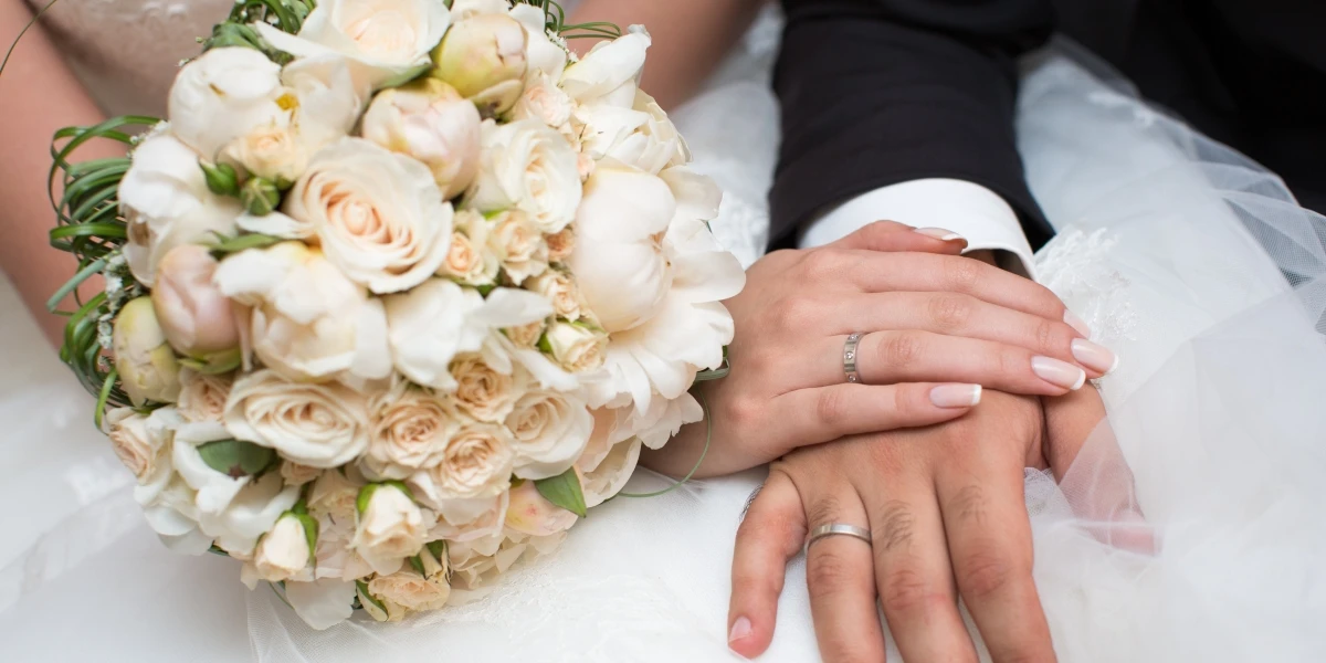 Newlywed couple showing wedding rings and bridal bouquet after marriage ceremony